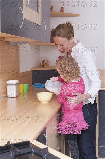 Mother helping daughter (4-5) pour milk into bowl