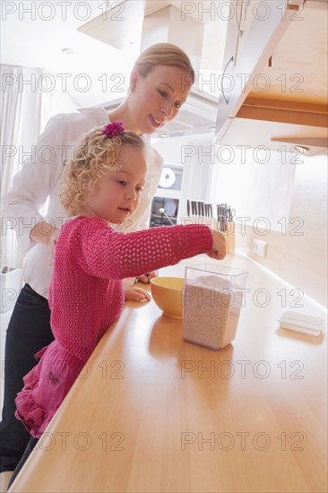 Mother watching daughter (4-5) taking out porridge from container