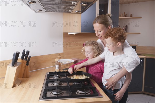 Mother, daughter (4-5) and son (8-9) preparing scrambled eggs together