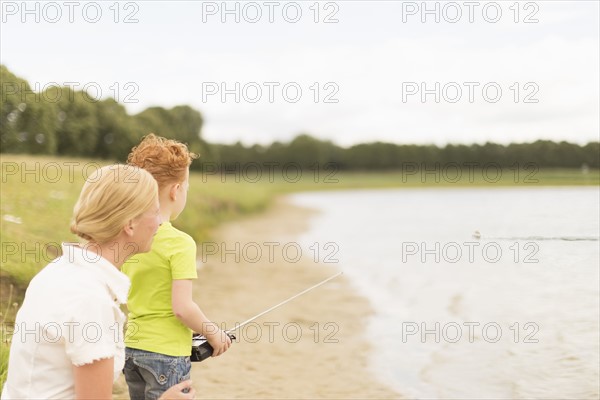Mother and son (8-9) playing with radio controlled motorboat on lake