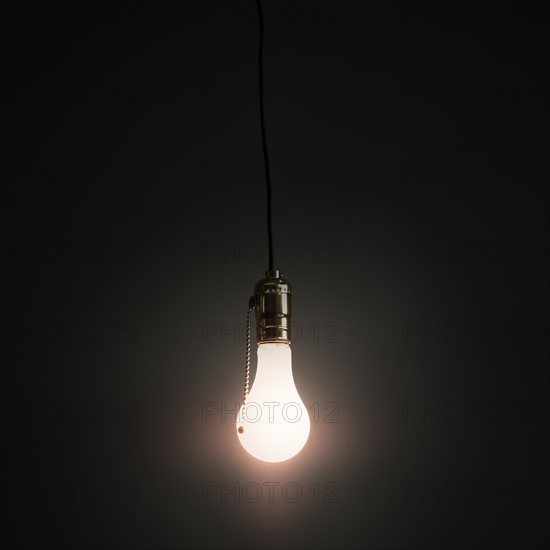 Light bulb hanging against grey background.