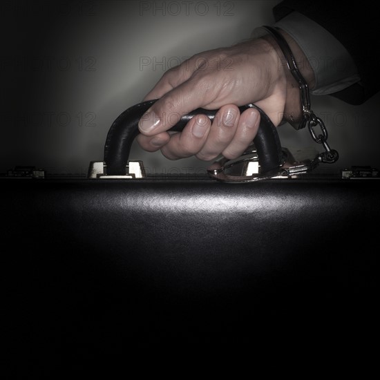 Hand connected to briefcase with handcuffs.