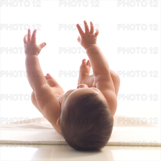 Naked baby girl (6-11 months) lying on back and reaching up.