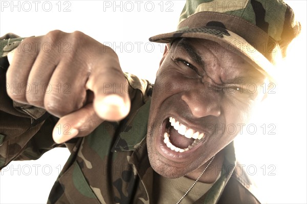 Portrait of man wearing camouflage clothing, screaming and pointing towards camera.