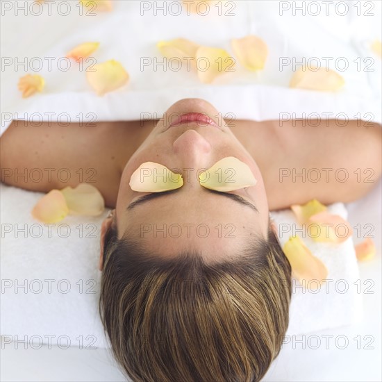 Mid adult woman lying on back under sheet covered with rose petals.