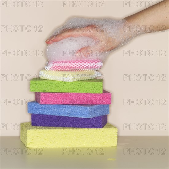 Female hand covered in foam on stack of sponges.