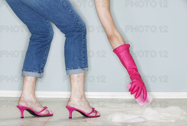 Legs and hand of mature woman wearing high heels and cleaning floor.
