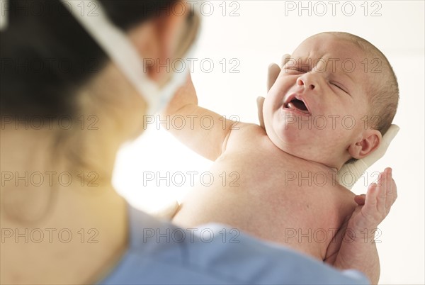 Woman in surgical mask holding crying baby girl (2-5 months).