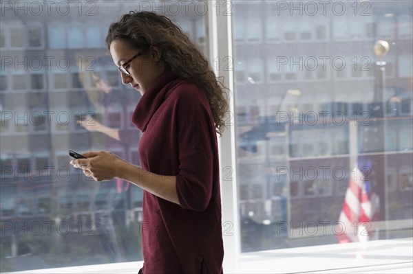 Young woman using mobile phone in front of window.