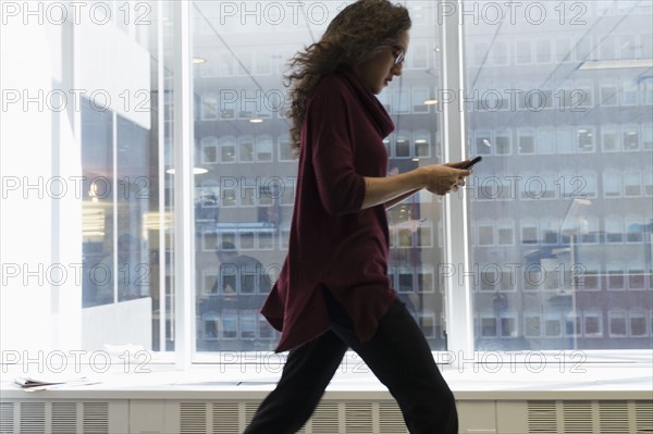 Young woman walking with mobile phone in front of window.