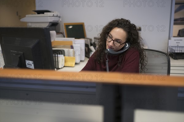 Young woman in cubicle talking via telephone.