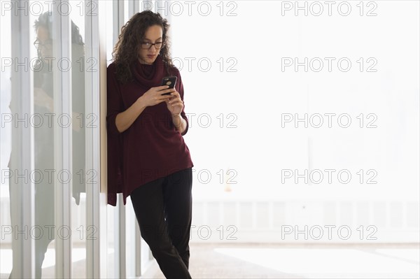 Young woman leaning on glass wall and text messaging.