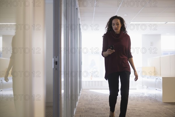 Young woman walking in corridor with mobile phone.