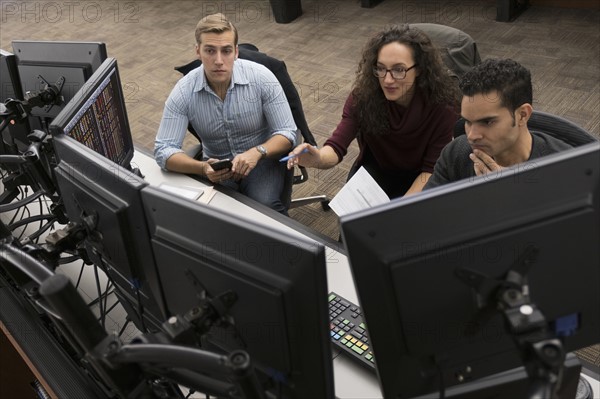 Young traders at meeting in front of computer monitors.