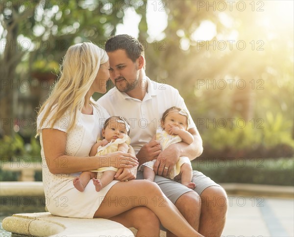 Happy family with two baby girls (2-5 months) at park in sunlight