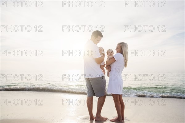 Happy family with two baby girls (2-5 months) at beach in sunlight