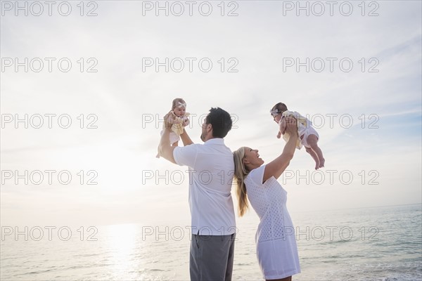 Happy family with two baby girls (2-5 months) at beach in sunlight