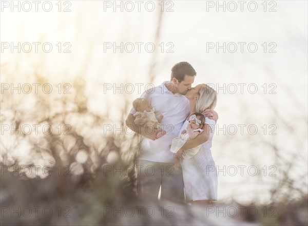 Couple with twins (2-5 months) kissing and holding