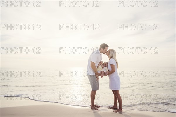 Couple with twins (2-5 months) kissing on seashore