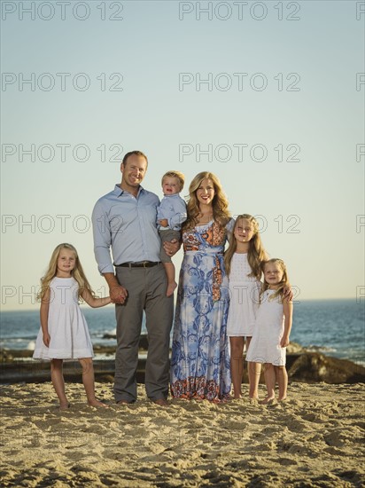 Family with children (12-17 months, 4-5, 6-7, 8-9) standing on beach with sea in background