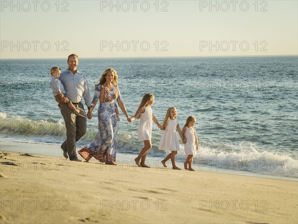 Family with children (12-17 months, 4-5, 6-7, 8-9) walking on beach with sea in background