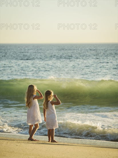 Girls (4-5, 6-7) standing on beach and looking at sea