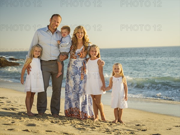 Family with children (12-17 months, 4-5, 6-7, 8-9) standing on beach with sea in background