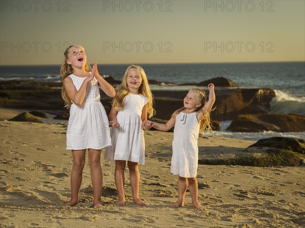 Girls (4-5, 6-7, 8-9) standing on beach with sea in background