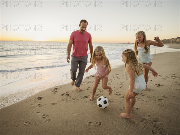 Father with children (4-5, 6-7, 8-9) playing soccer on beach