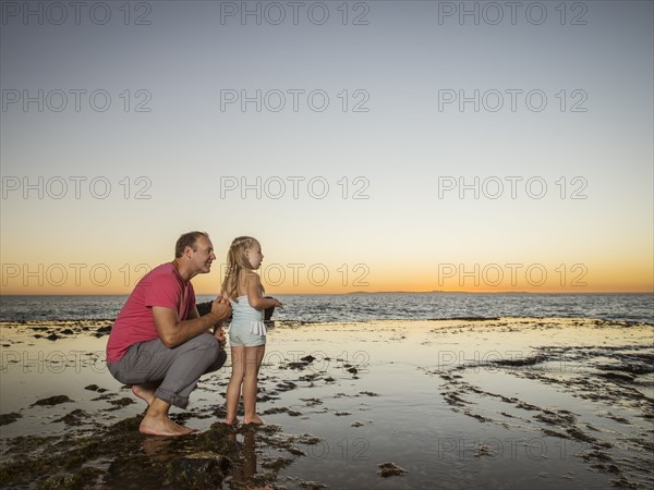 Father crouching next to daughter (4-5) on beach