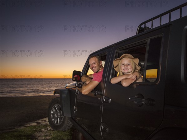 Father and daughter (4-5) sitting in car on beach