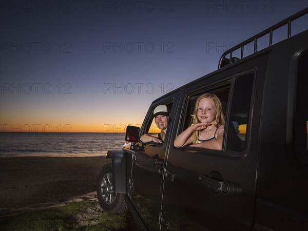 Mother and daughter (4-5) sitting in car on beach