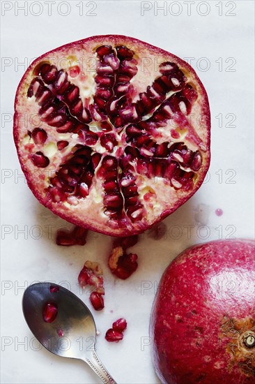 Halved Pomegranate and spoon against white background