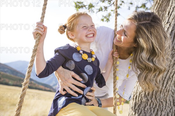 Mother with girl (4-5) sitting on swing