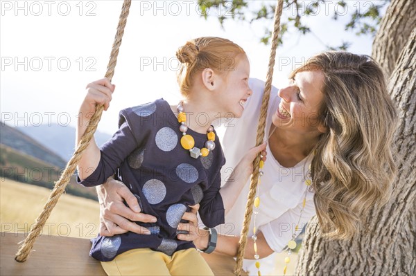 Mother with girl (4-5) sitting on swing