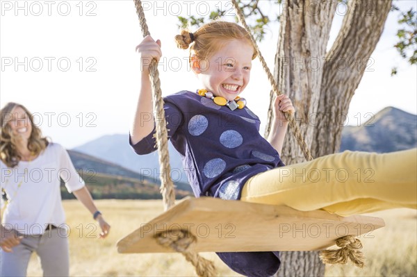 Mother with girl (4-5) sitting on swing