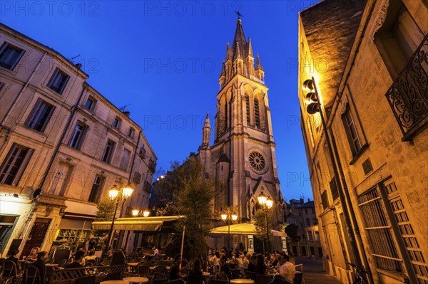 France, Occitanie, Montpellier, Sidewalk cafe and St. Anne Church at dusk