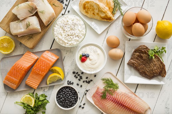 Chicken meat, fish, cottage cheese, yogurt and eggs on white table