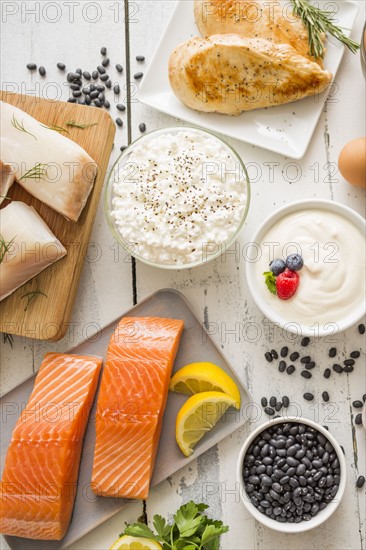 Chicken meat, fish, cottage cheese, yogurt and eggs on white table