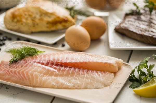 Raw tilapia fish on plate, chicken and eggs in background