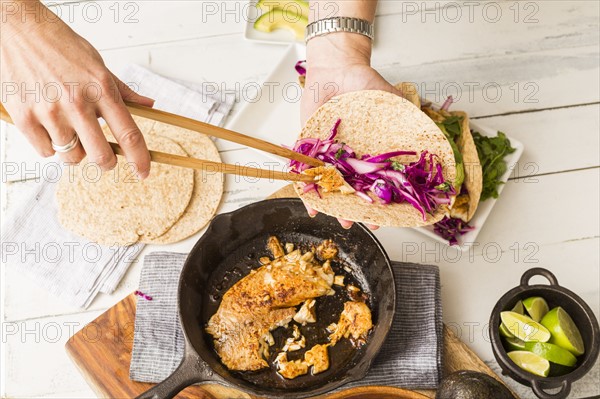 Woman preparing tortilla with tilapia and red cabbage