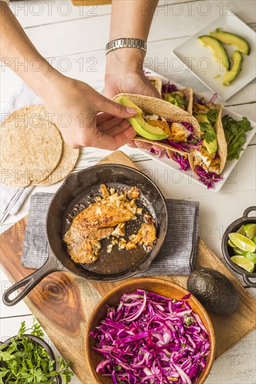 Woman preparing tortilla with tilapia, avocado and red cabbage
