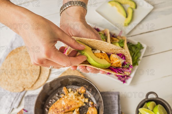 Woman preparing tortilla with tilapia, avocado and red cabbage