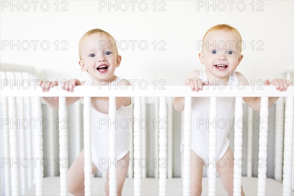 Twin brothers (12-17 months) standing in crib