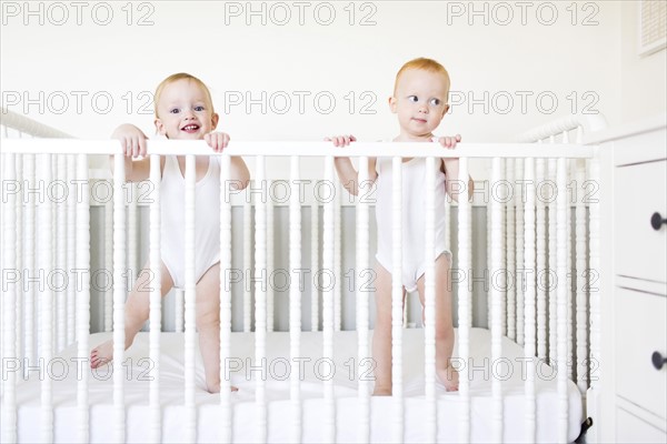Twin brothers (12-17 months) standing in crib