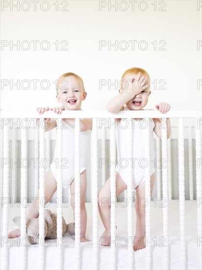 Twin brothers (12-17 months) standing in crib