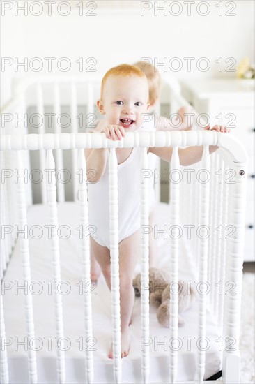 Twin brothers (12-17 months) standing in crib