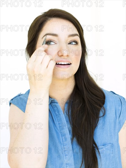 Woman wearing blue top tweezing eyebrow