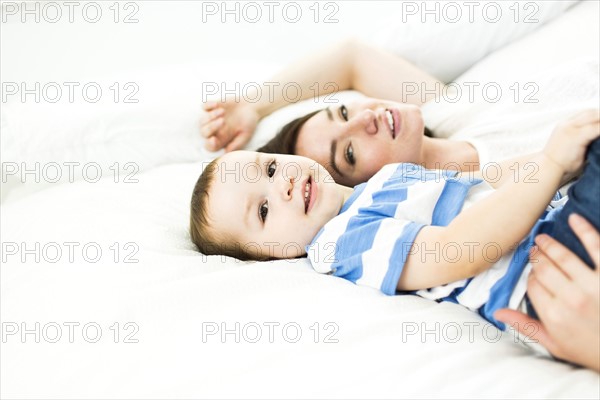 Mother lying with son (4-5) on bed and smiling