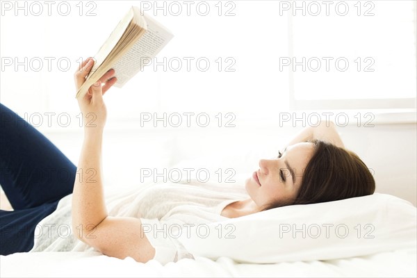 Woman lying on bed and reading book